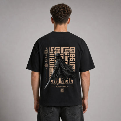 A man viewed from behind wearing a black t-shirt with a large graphic print on the back. The graphic features a dark knight in a flowing cape holding a sword, set against a beige geometric maze and Arabic calligraphy.