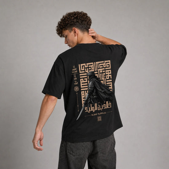 A man wearing a black t-shirt with a large gold and black graphic print on the back, shown from behind against a neutral gray studio background.