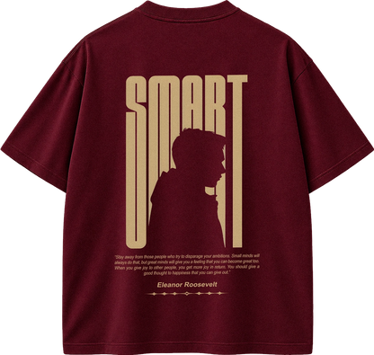 A maroon short-sleeve t-shirt shown from the back, featuring a large gold graphic print with the word 'SMART' in a vertical stylized font, a silhouette of a person, and a quote attributed to Eleanor Roosevelt.