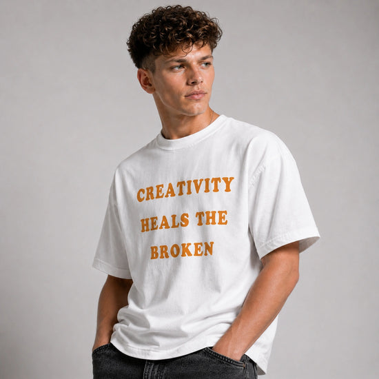 Man wearing a white t-shirt with 'CREATIVITY HEALS THE BROKEN' text on a gray background