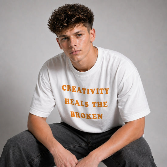 Person wearing a white t-shirt with 'Creativity Heals the Broken' text on a gray background