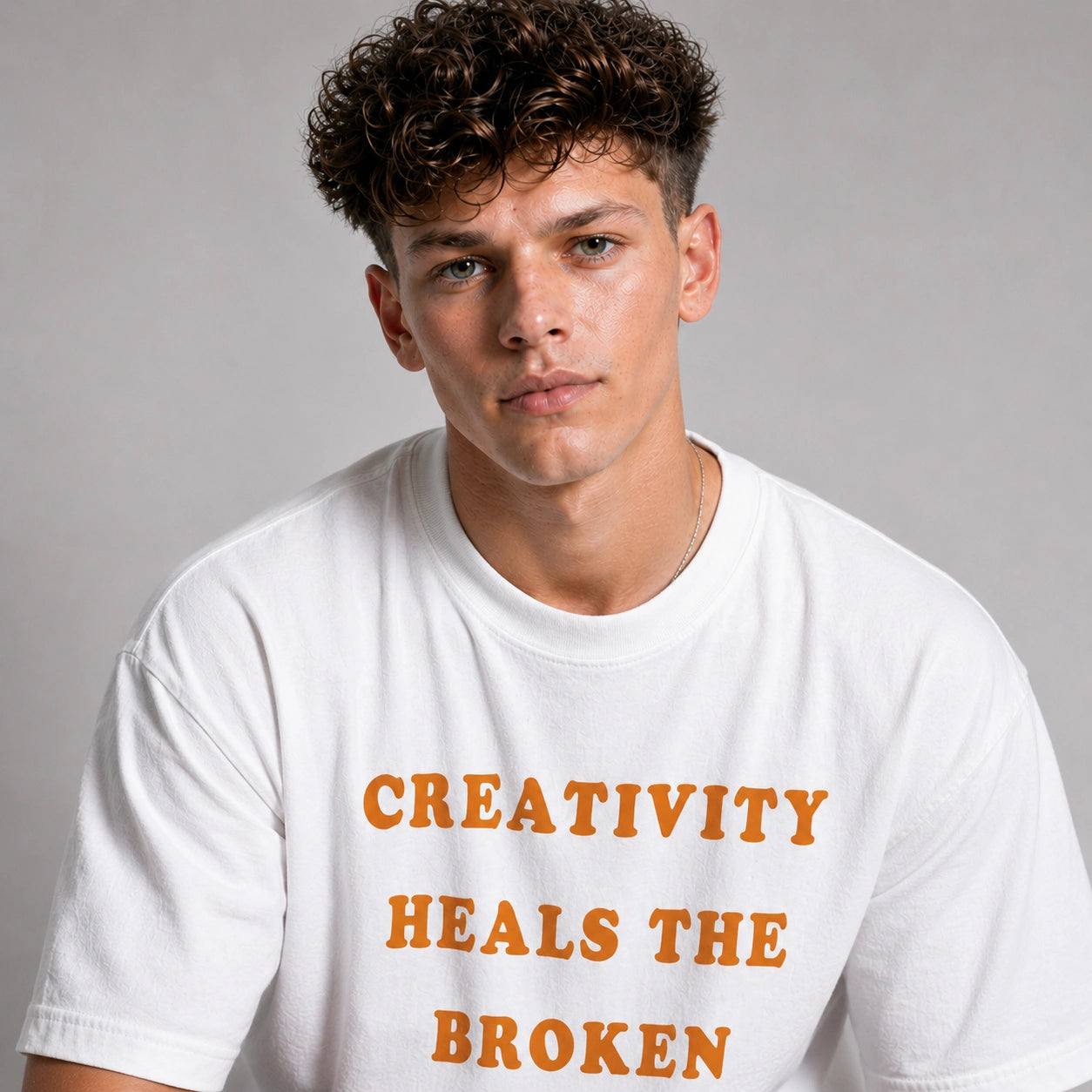 Person wearing a white t-shirt with 'Creativity Heals the Broken' text in orange.