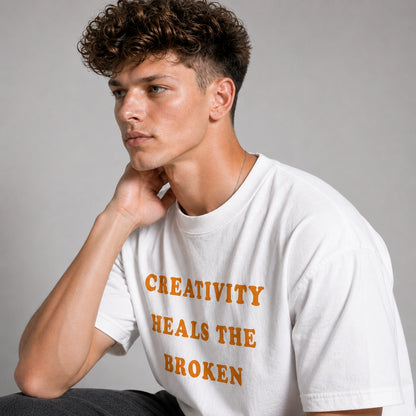 Man wearing a white t-shirt with 'Creativity Heals the Broken' text in orange on a gray background