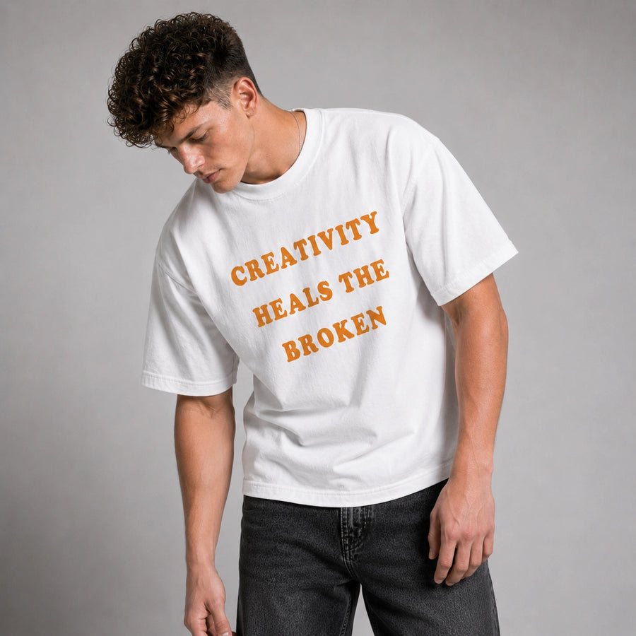 Person wearing a white t-shirt with 'Creativity Heals the Broken' text on a gray background