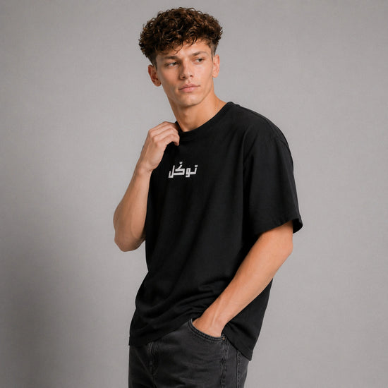 Man wearing a black t-shirt with Arabic text on a gray background