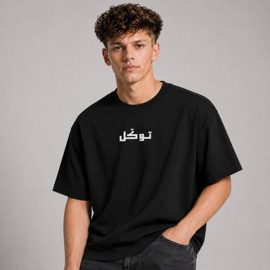 Person wearing a black t-shirt with Arabic text on a gray background