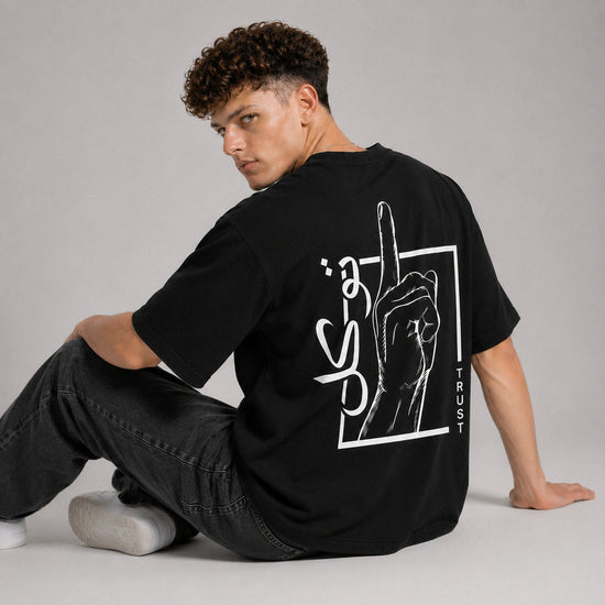 Person wearing a black t-shirt with a graphic design on the back, sitting against a gray background.