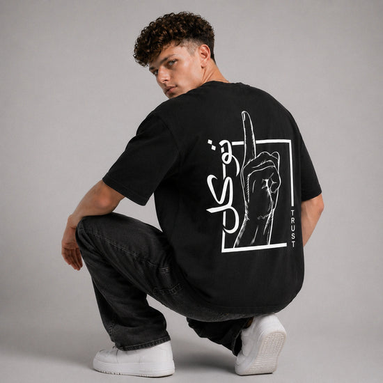 Person wearing a black t-shirt with a graphic design on the back, sitting against a gray background
