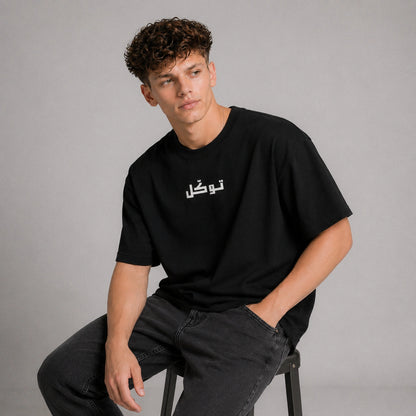 Person wearing a black t-shirt with white text sitting on a stool against a gray background