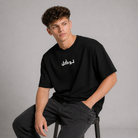 Person wearing a black t-shirt with white text sitting on a stool against a gray background