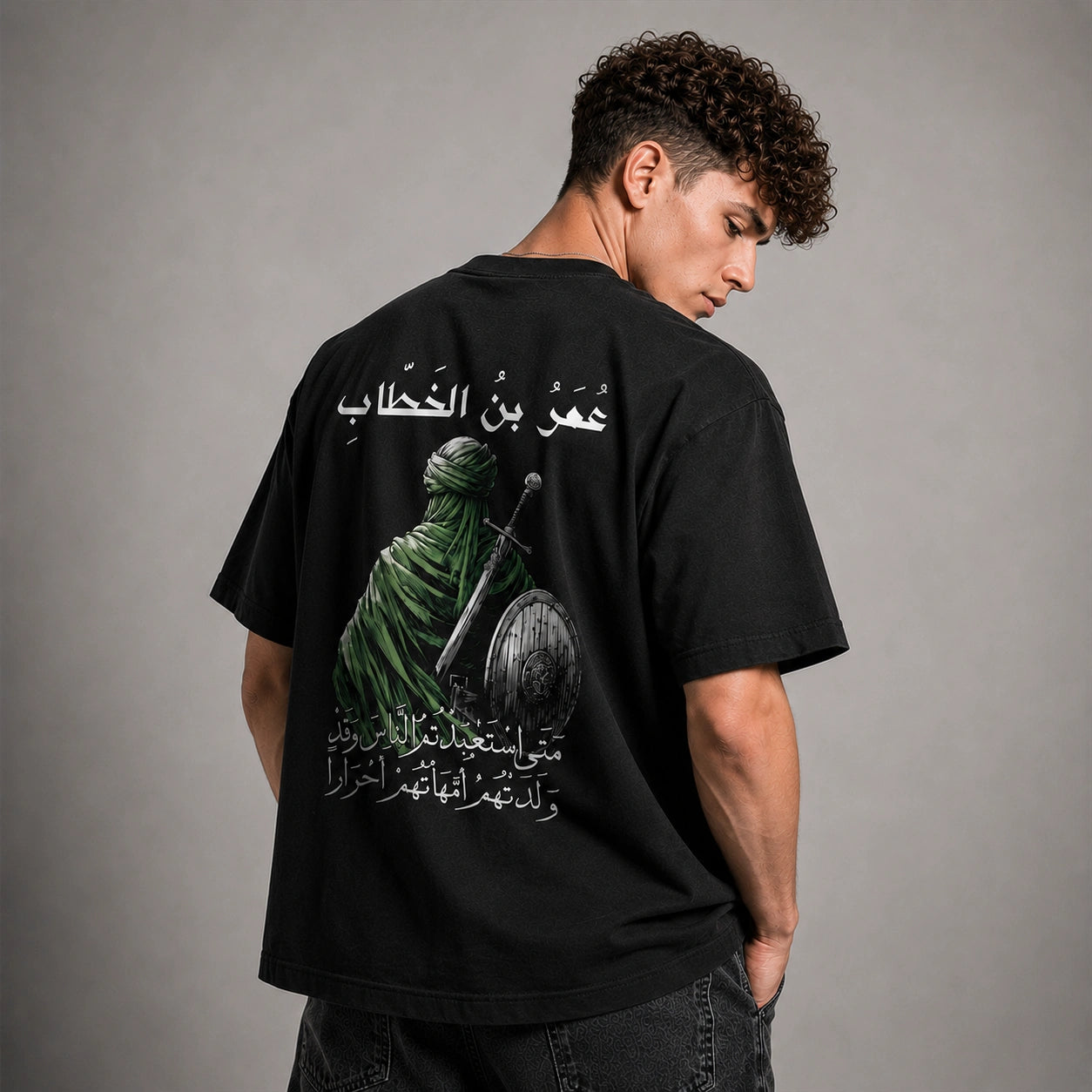A man wearing a black t-shirt with a large graphic print on the back, photographed from behind against a neutral gray studio background.