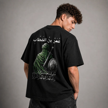 A man wearing a black t-shirt with a large graphic print on the back, photographed from behind against a neutral gray studio background.