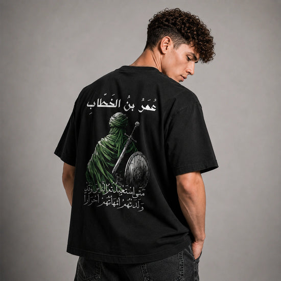 A man wearing a black t-shirt with a large graphic print on the back, photographed from behind against a neutral gray studio background.