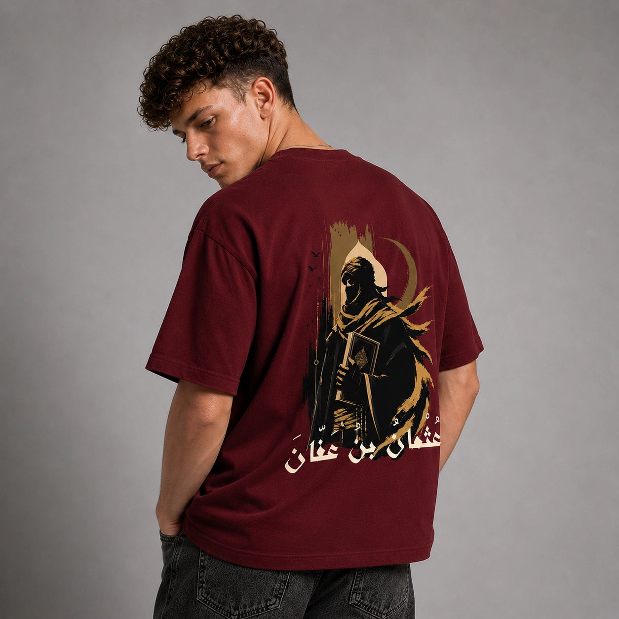 A man wearing a maroon t-shirt with a large graphic print on the back, shown from behind against a gray studio background.