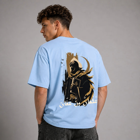 A man wearing a light blue t-shirt with a large graphic print on the back, shown from behind against a neutral gray studio background.