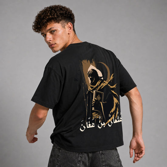 A man wearing a black t-shirt with a large graphic print on the back, photographed from behind against a neutral gray studio background.