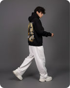 Person wearing a black hoodie with a graphic design, white pants, and white shoes on a gray background