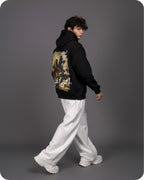 Person wearing a black hoodie with a graphic design on the back, white pants, and white shoes against a gray background