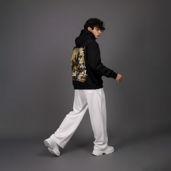 Person wearing a black hoodie with a graphic design and white pants on a gray background