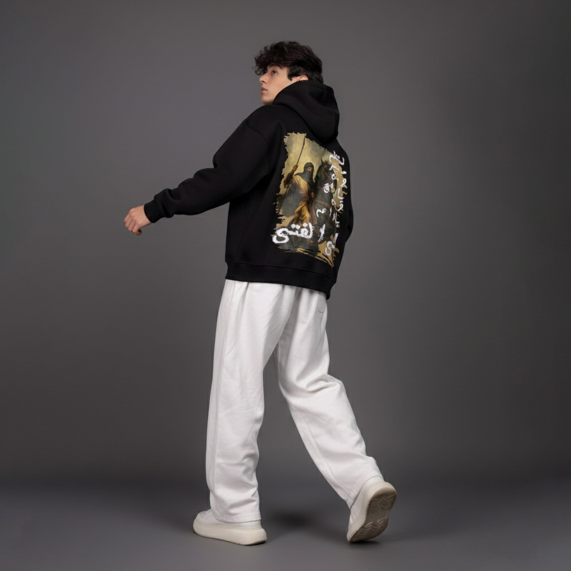 Person wearing a black hoodie with a graphic design on the back against a gray background