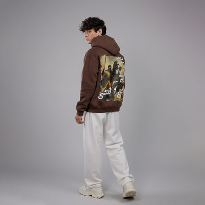 Person wearing a brown hoodie with graphic designs on the back against a gray background