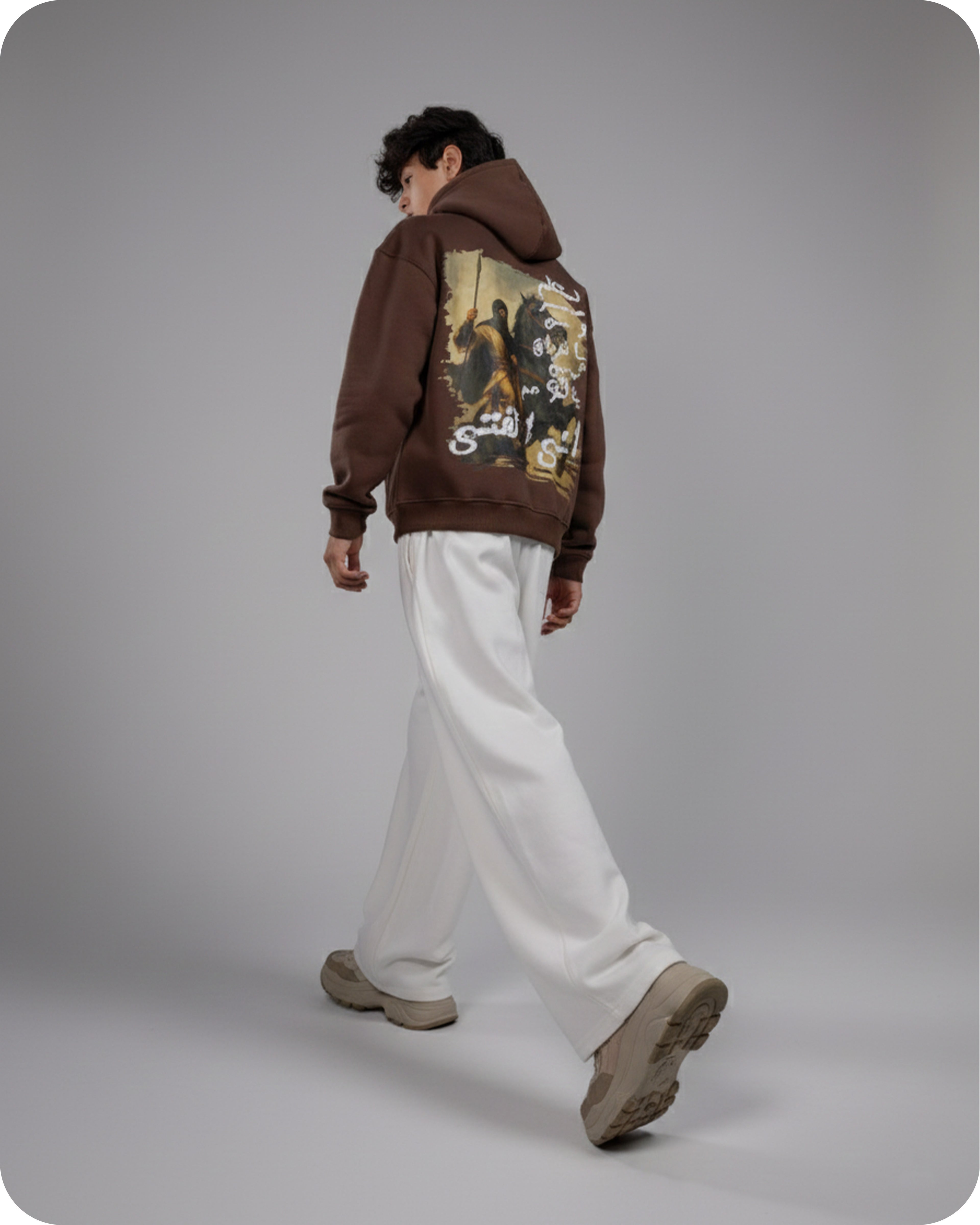 Person wearing a brown hoodie with a graphic design on the back, standing against a gray background