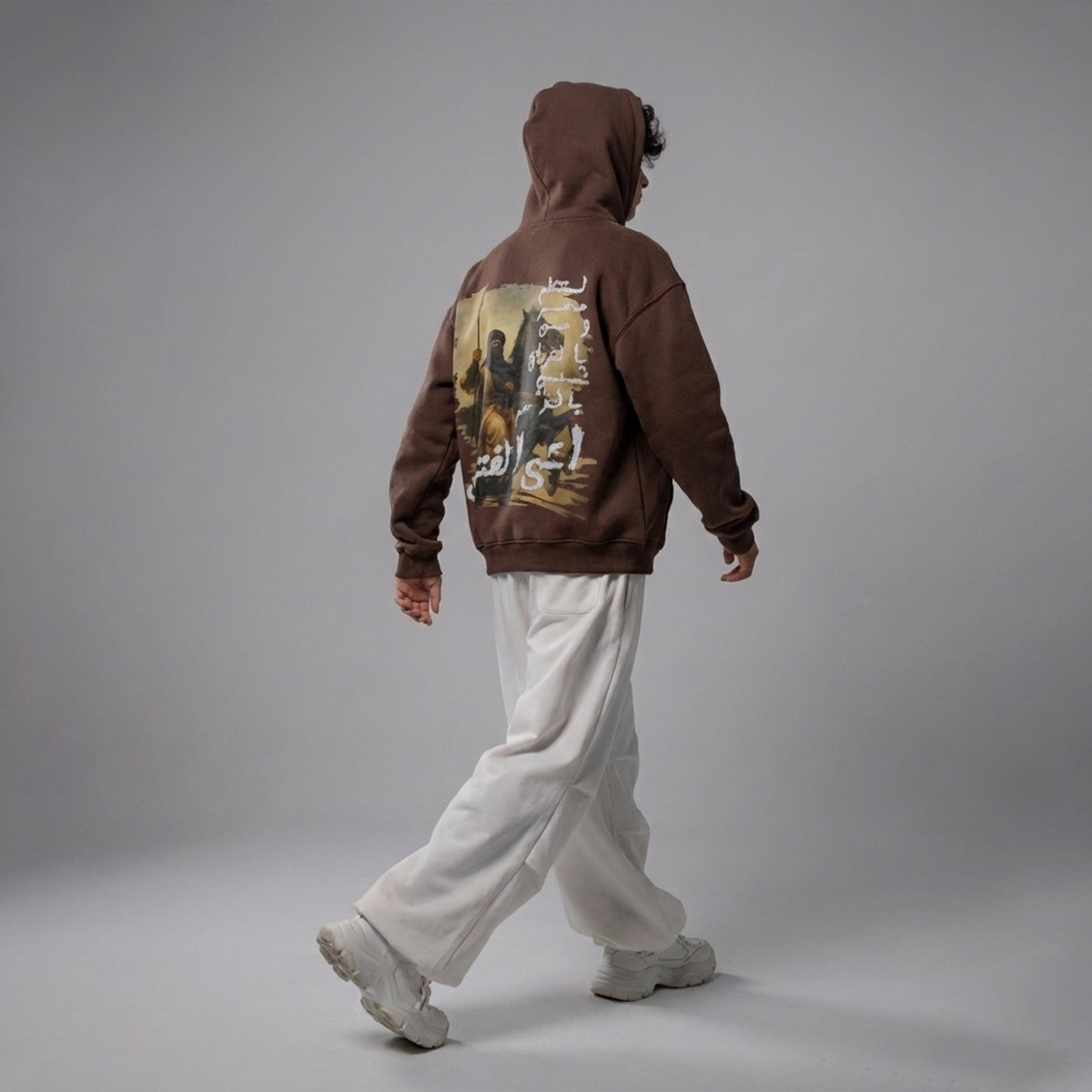 Person wearing a brown hoodie with a graphic design on the back against a gray background