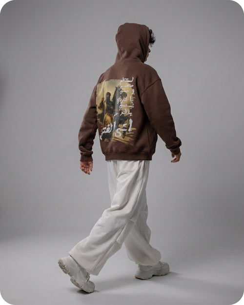 Person wearing a brown hoodie with a graphic design on the back against a gray background