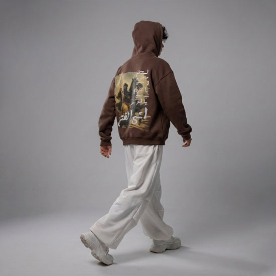 Person wearing a brown hoodie with a graphic design on the back against a gray background