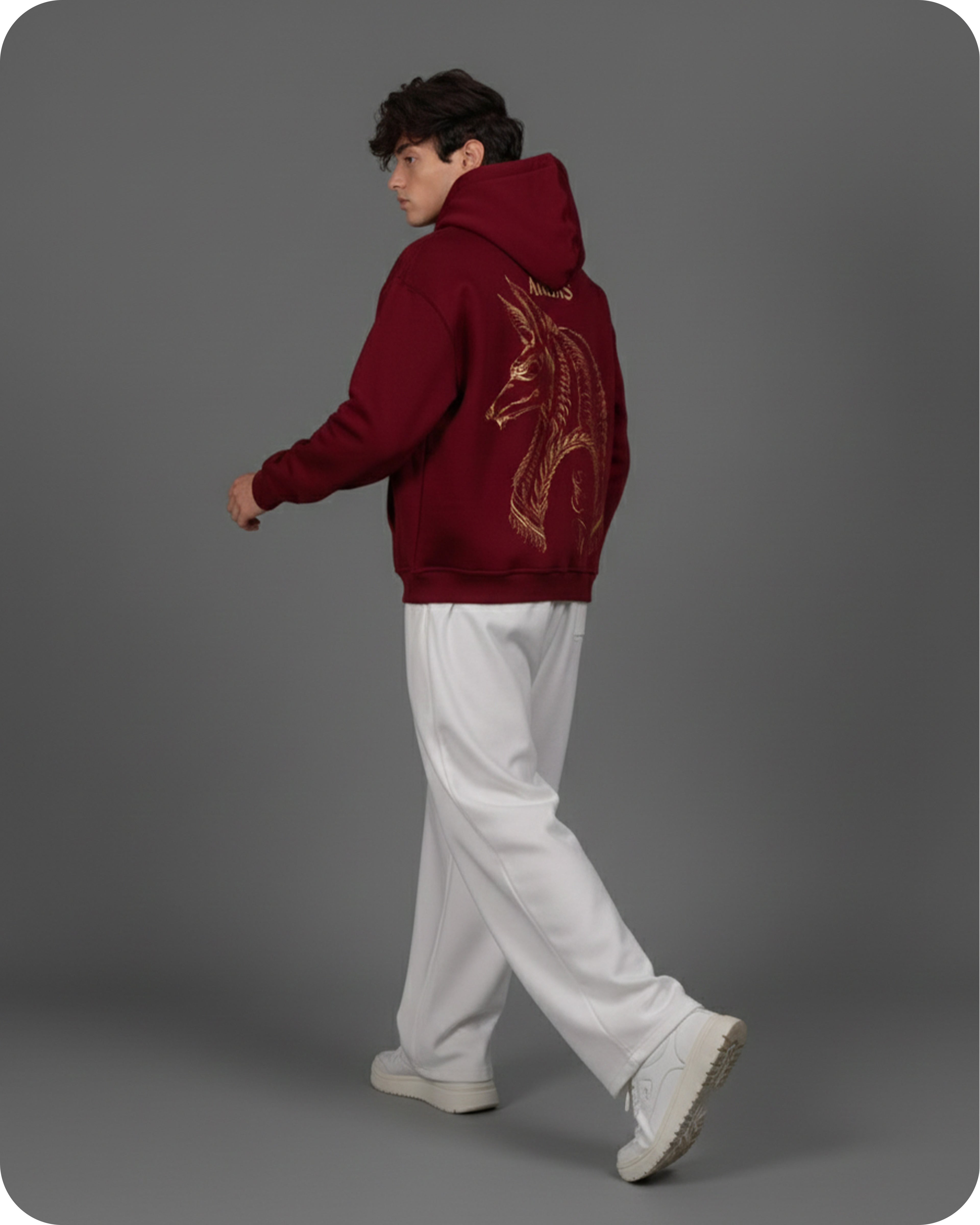 Person wearing a maroon hoodie with a dragon design on the back, standing against a gray background.