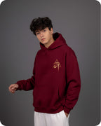 Person wearing a maroon hoodie with a logo on a gray background