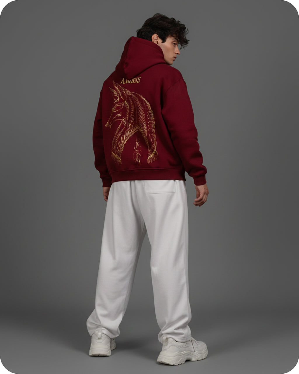 Person wearing a maroon hoodie with a dragon design on the back, standing against a gray background.