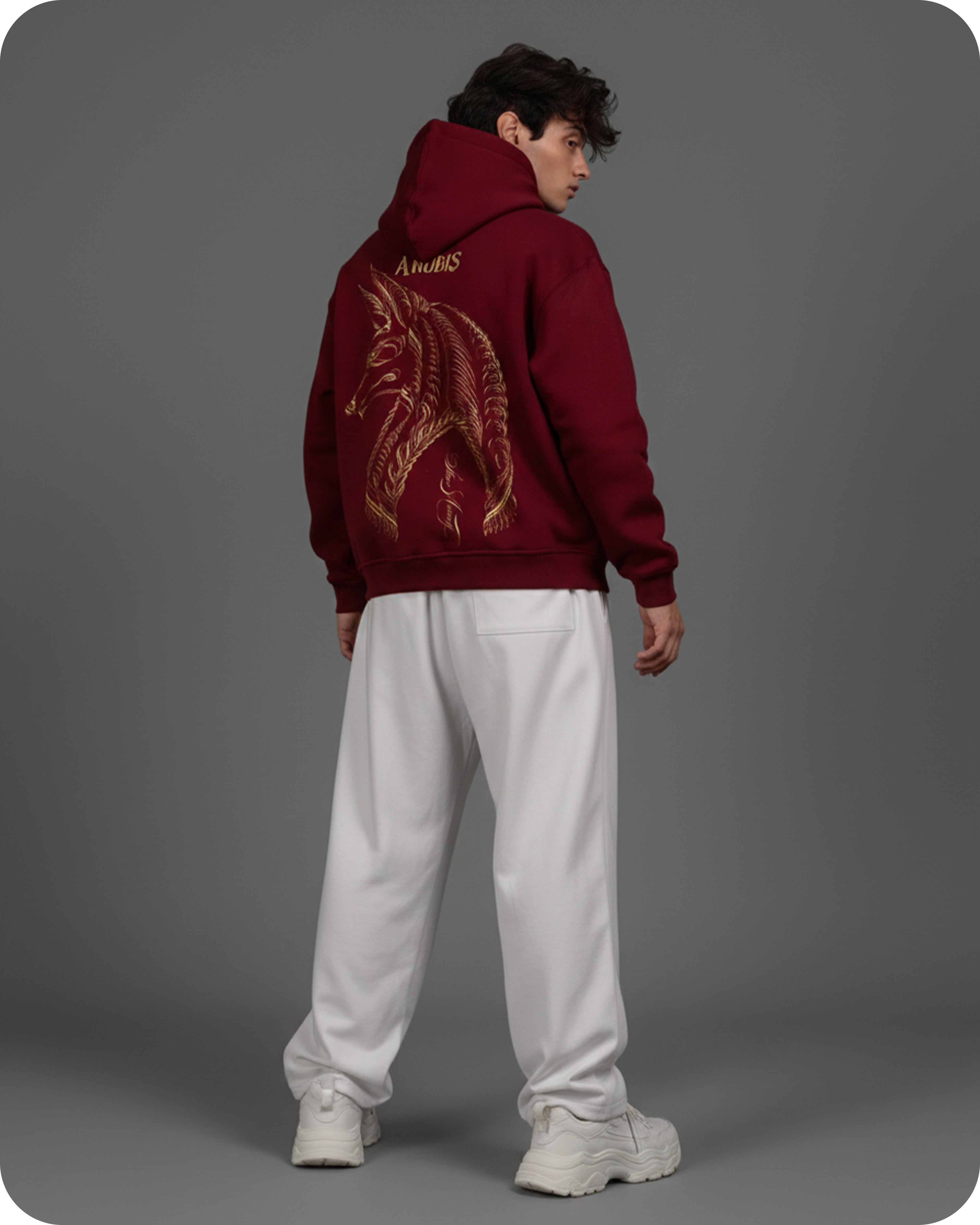 Person wearing a maroon hoodie with a dragon design on the back, standing against a gray background.