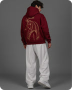 Person wearing a maroon hoodie with a gold dragon design on the back, standing against a gray background.