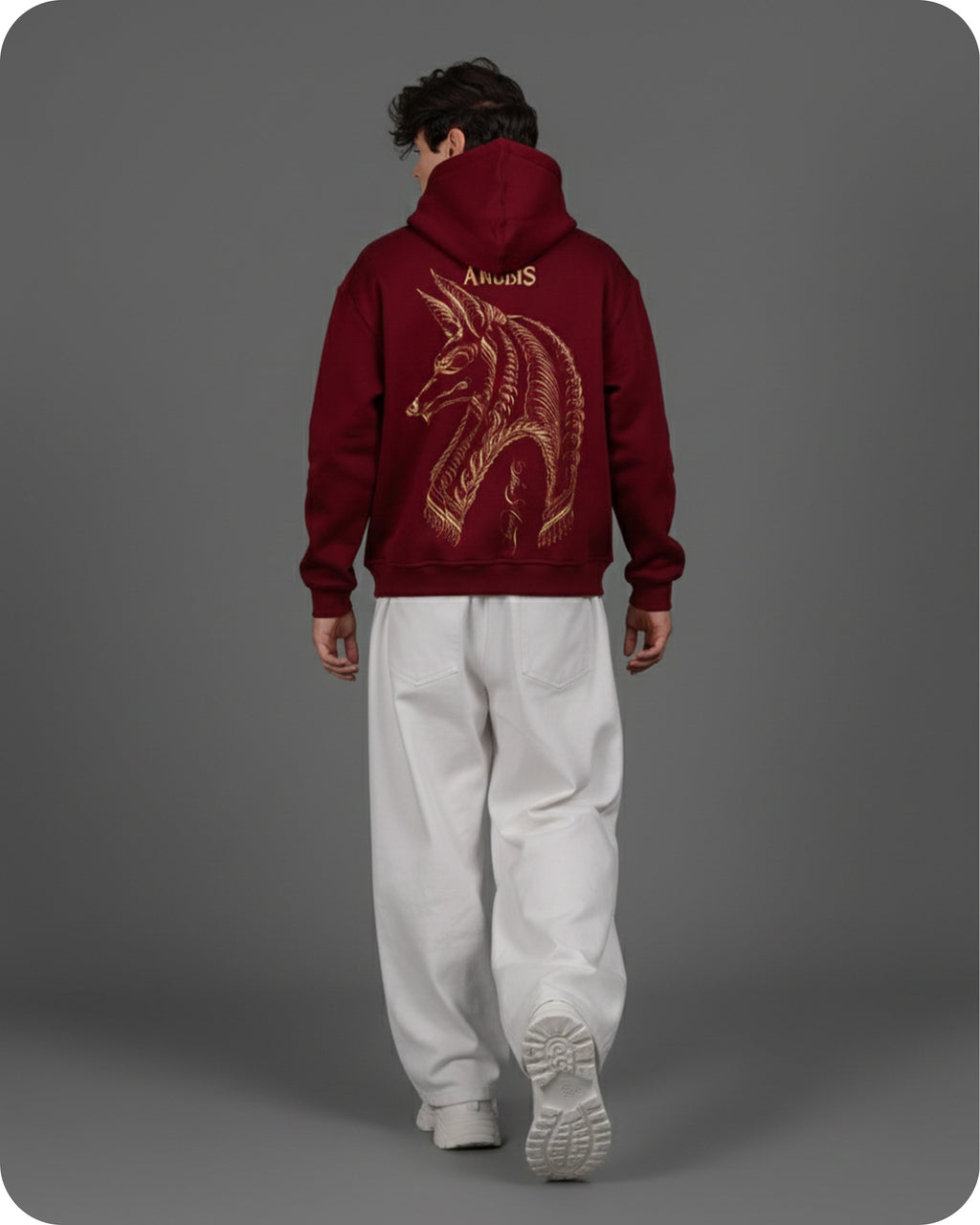 Person wearing a maroon hoodie with a gold design on the back against a gray background