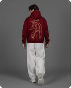 Person wearing a maroon hoodie with a gold design on the back against a gray background