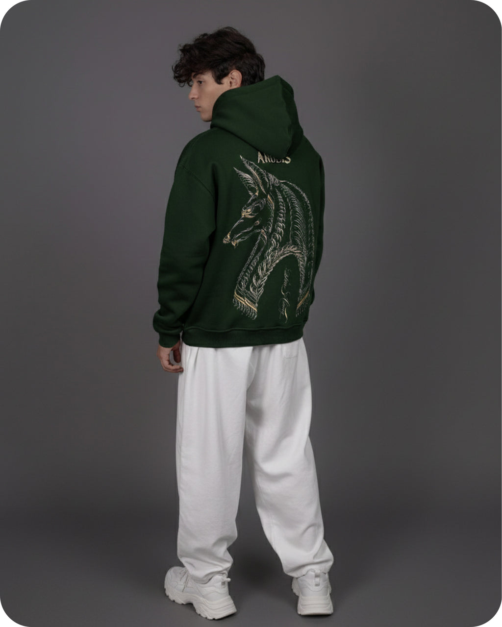 Person wearing a green hoodie with a dragon design on the back, standing against a gray background