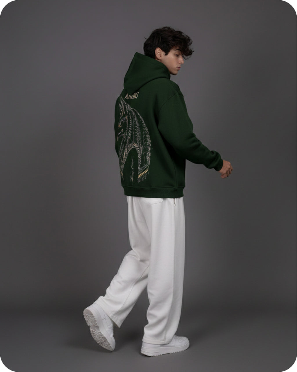 Person wearing a green hoodie with a dragon design on the back, standing against a gray background