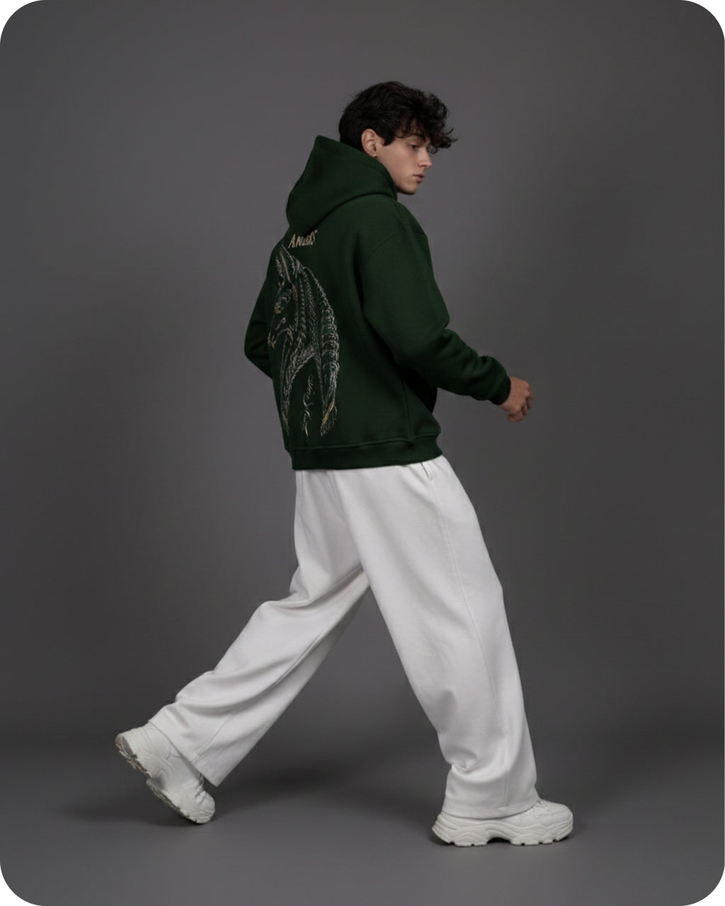 Person wearing a green hoodie with a dragon design and white pants on a gray background
