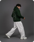 Person wearing a green hoodie with a dragon design and white pants on a gray background