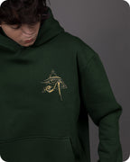 Person wearing a green hoodie with a gold embroidered symbol on a gray background