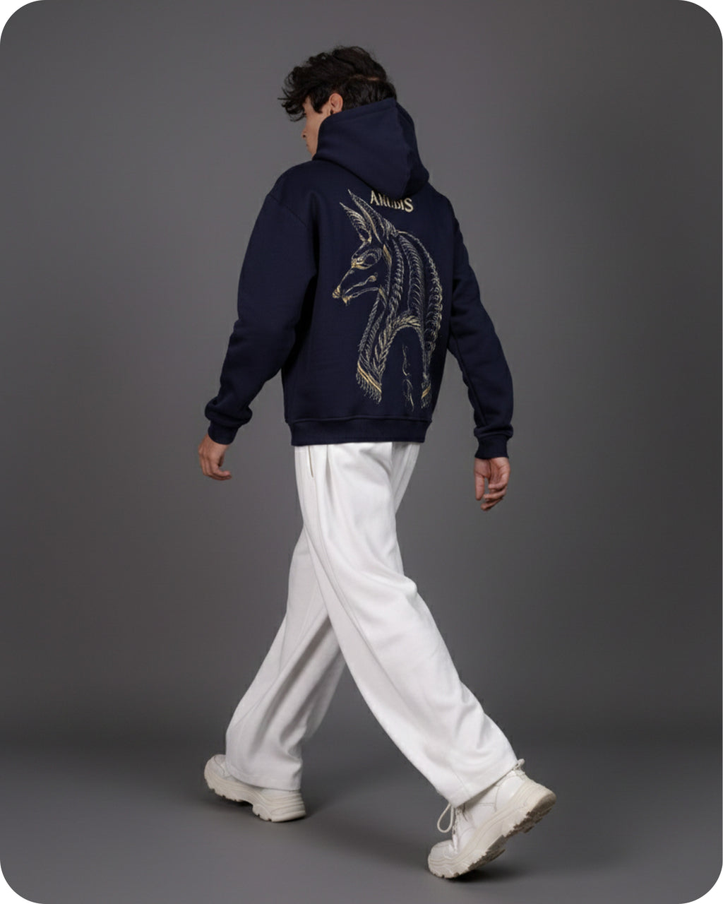Person wearing a navy hoodie with a dragon design on the back, walking against a gray background