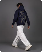 Person wearing a navy hoodie with a dragon design on the back, walking against a gray background