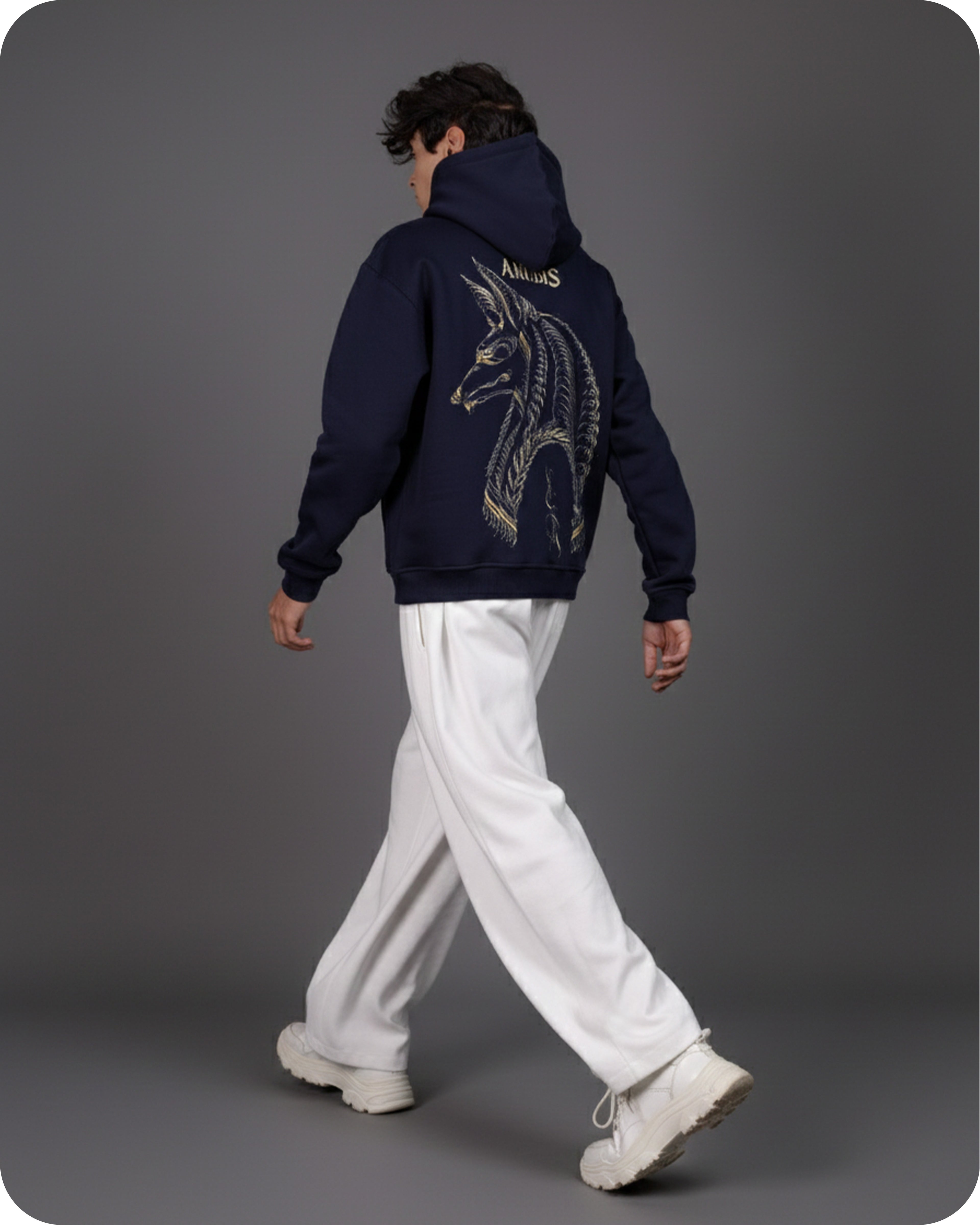 Person wearing a navy hoodie with a dragon design on the back, walking against a gray background