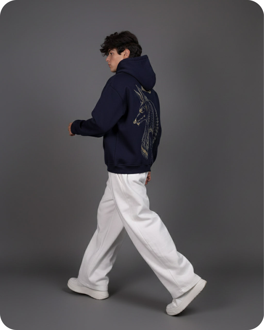 Person wearing a dark blue hoodie with a design on the back, walking against a gray background