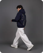 Person wearing a dark blue hoodie with a design on the back, walking against a gray background