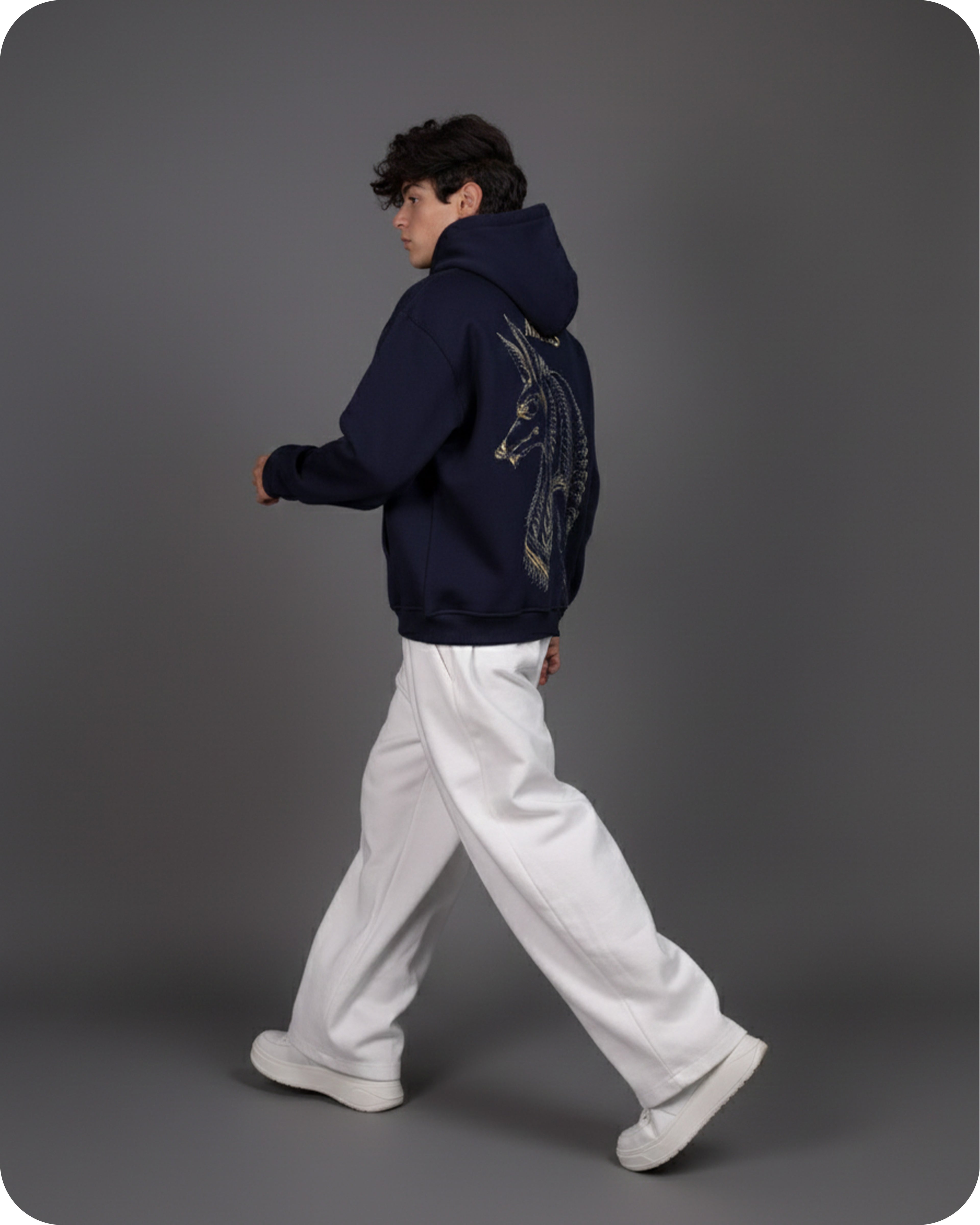 Person wearing a dark blue hoodie with a design on the back, walking against a gray background