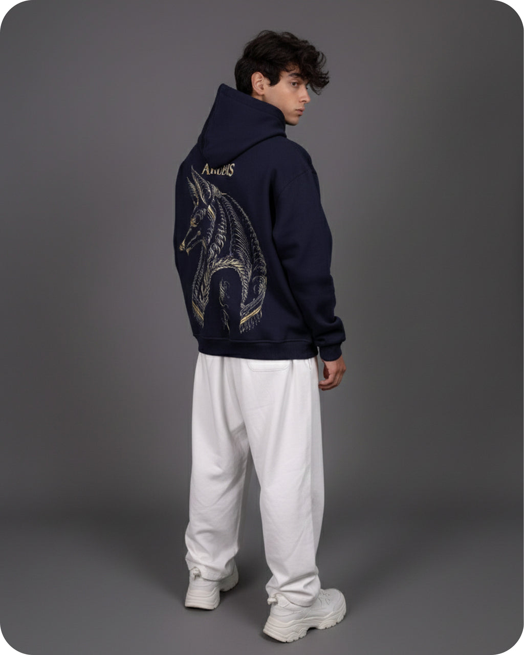 Person wearing a navy hoodie with a unicorn design on the back, standing against a gray background