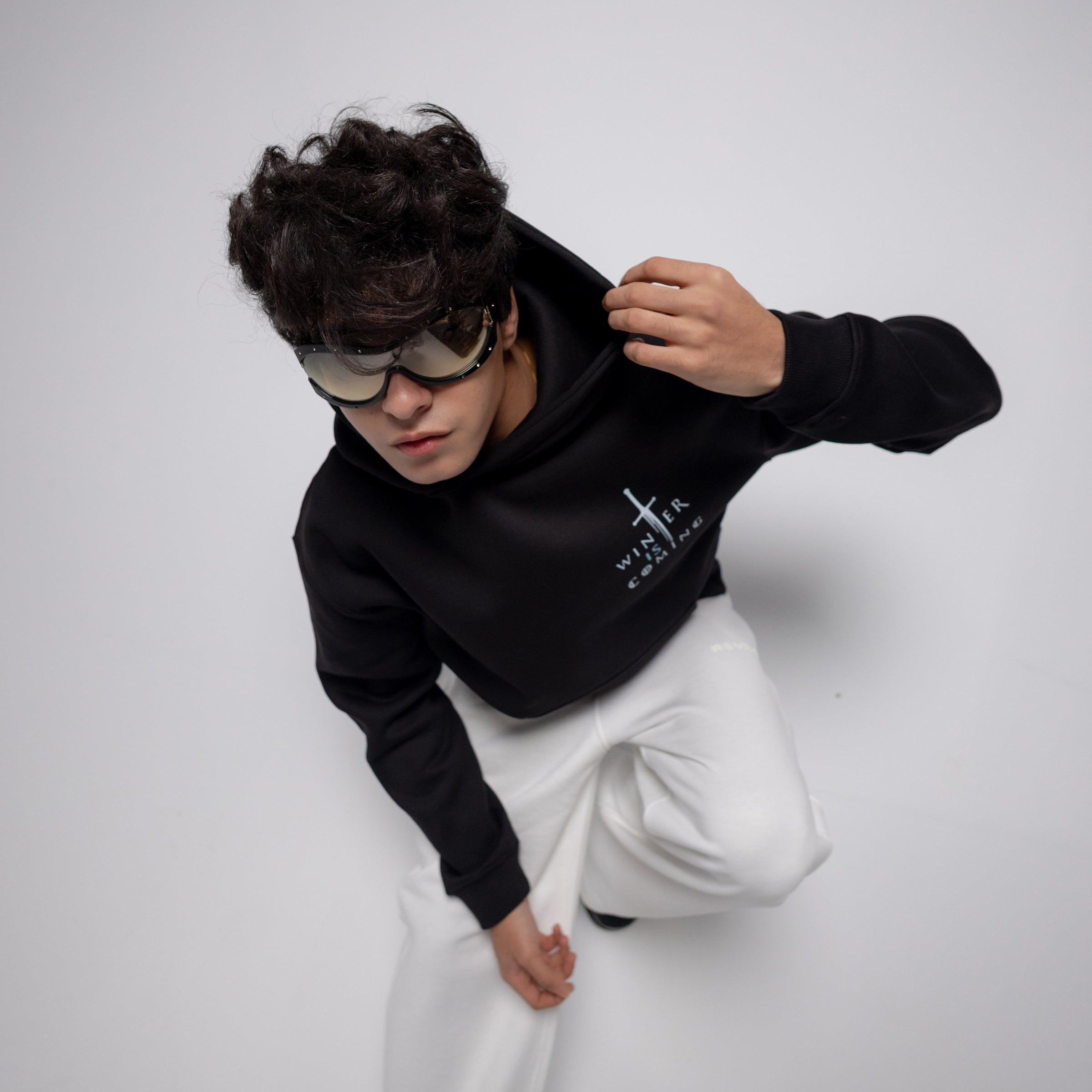 Person wearing a black hoodie with a logo and white pants on a light gray background