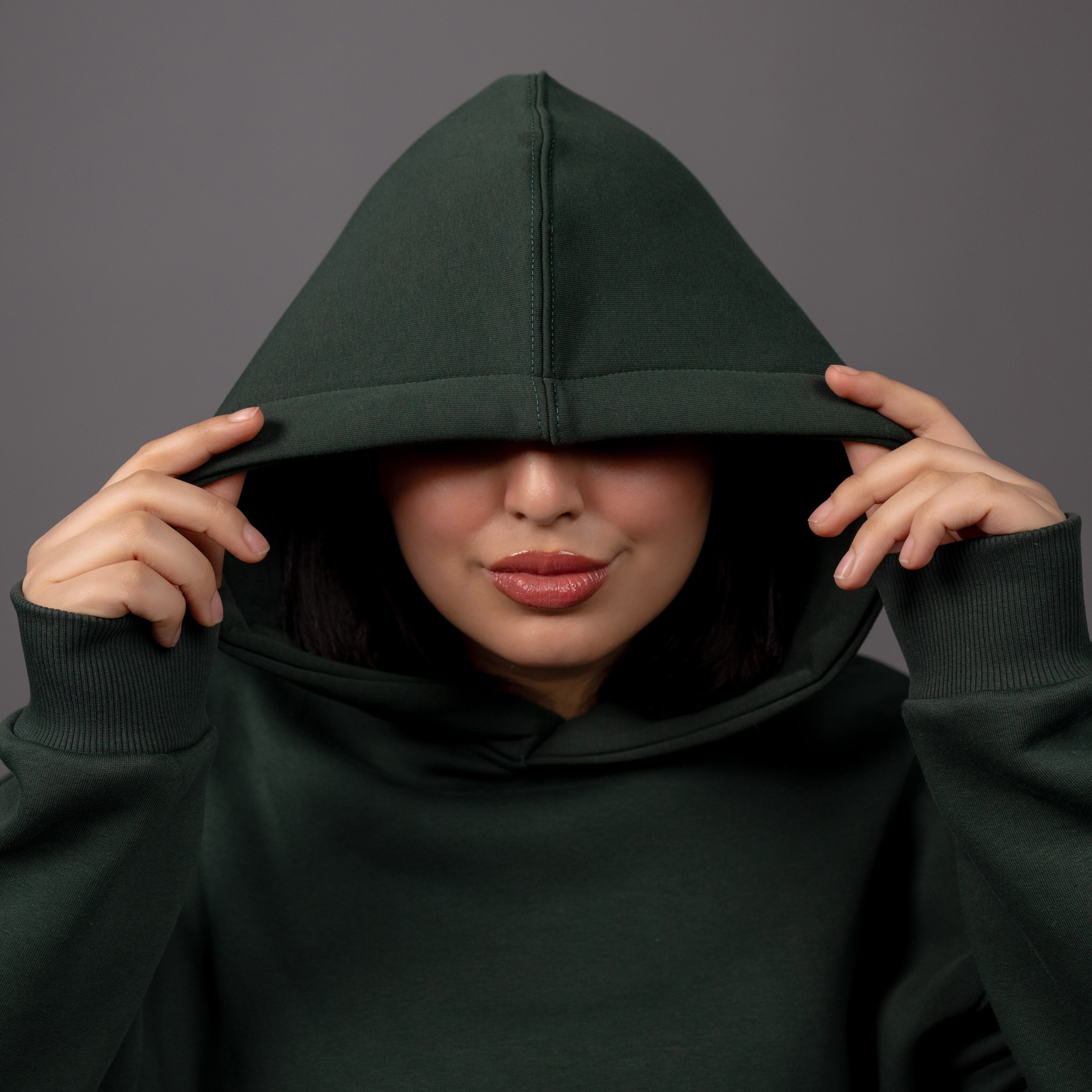 Person wearing a dark green hoodie against a gray background